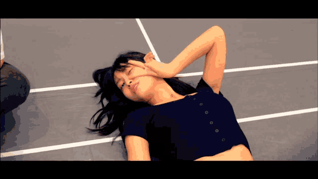 a woman in a black top is laying on the floor with her eyes closed