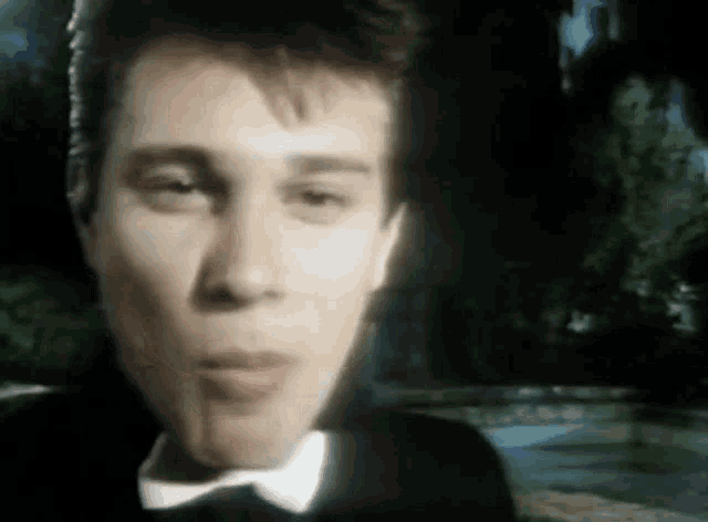 a man in a tuxedo and bow tie is standing in front of a pool .