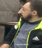 a man with a beard is wearing a yellow adidas jacket and a black shirt .