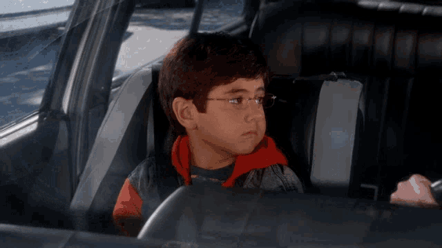 a young boy wearing glasses sits in a car