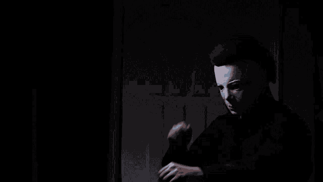 a man wearing a white mask is standing in a dark room