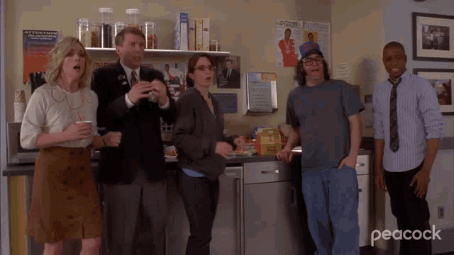 a group of people standing in a kitchen with peacock written on the bottom right