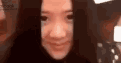 a close up of a woman 's face with long black hair smiling and looking at the camera .