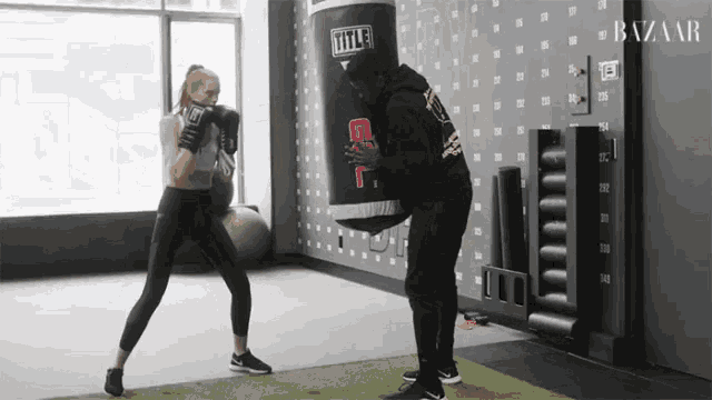 a man and a woman are boxing in a gym and the man is wearing a hoodie that says harper 's bazaar
