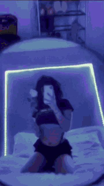 a girl is kneeling on a bed taking a selfie with her phone .