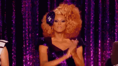 a drag queen is clapping her hands on a stage .