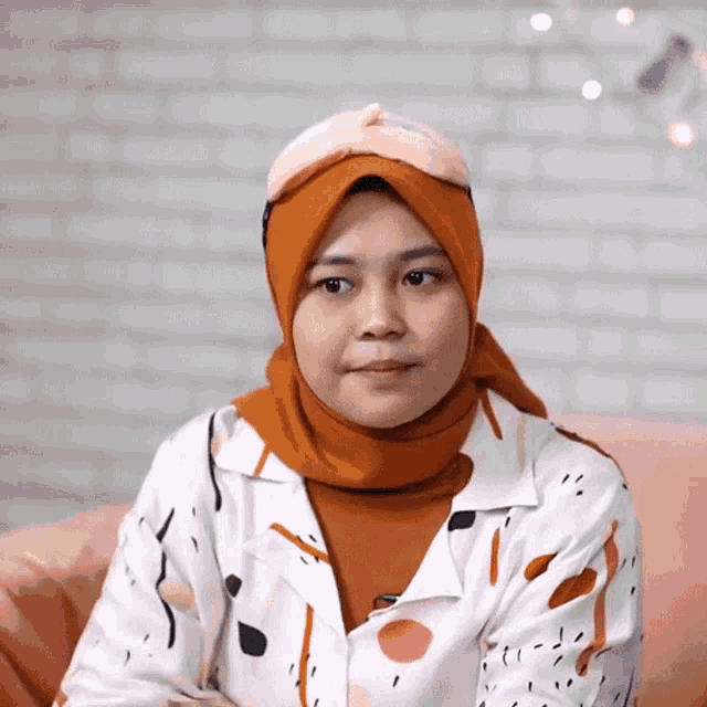 a woman wearing a headband and a hijab is sitting on a pink couch