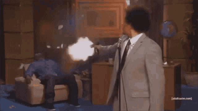 a man in a suit is pointing a gun at another man in a couch