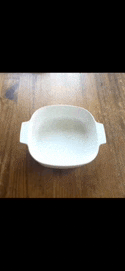 a white plate with two handles is sitting on a wooden table .