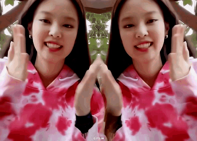 a woman in a pink tie dye sweatshirt is making a heart shape with her hands