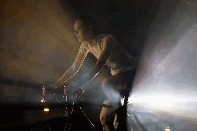 a woman in a white shirt is riding a bike in the dark