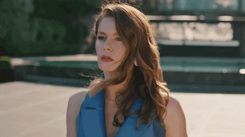 a woman in a blue dress looks at the camera with her hair blowing in the wind