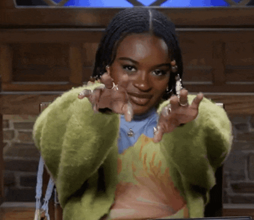 a woman in a green sweater is making a heart shape with her hands