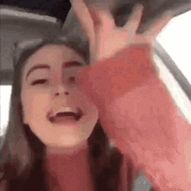 a woman in a pink sweater is sitting in a car with her hands in the air .