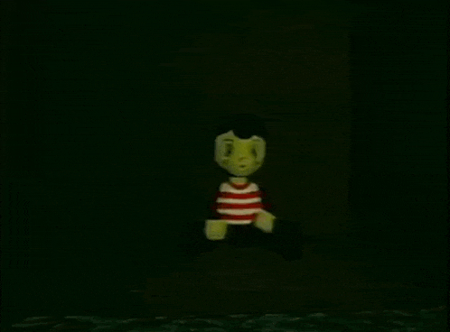 a cartoon character with a yellow face and a red and white striped shirt is waving in the dark .