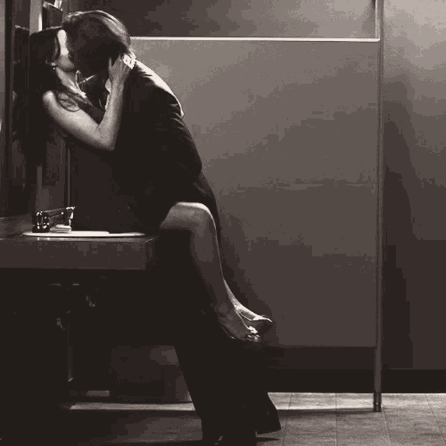 a black and white photo of a man and woman kissing on a bathroom sink