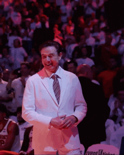 a man in a white suit and tie is smiling in front of a crowd with a sign that says event tickets
