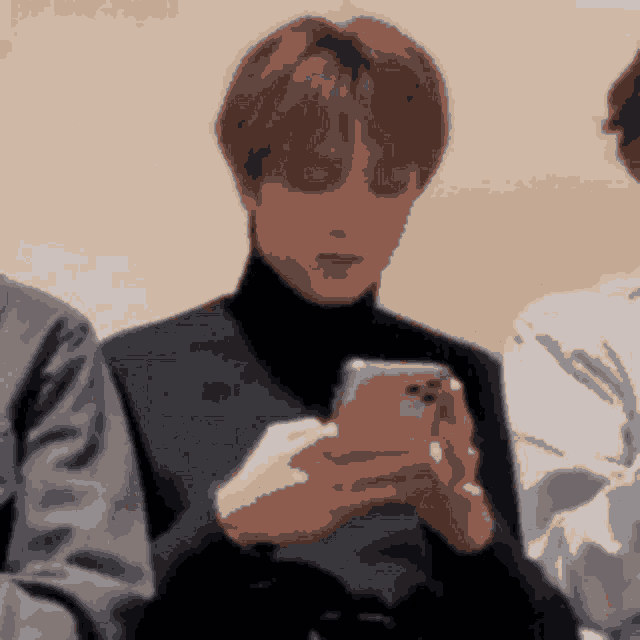 a man in a turtleneck is looking at his cell phone .