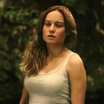 a woman in a white tank top is standing in the woods