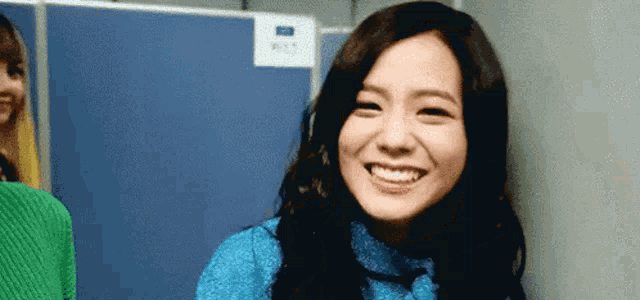 a woman in a blue sweater is smiling while standing next to another woman in a green sweater .
