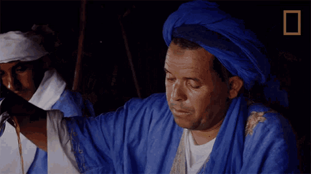 a man in a blue turban is standing in front of a national geographic sign