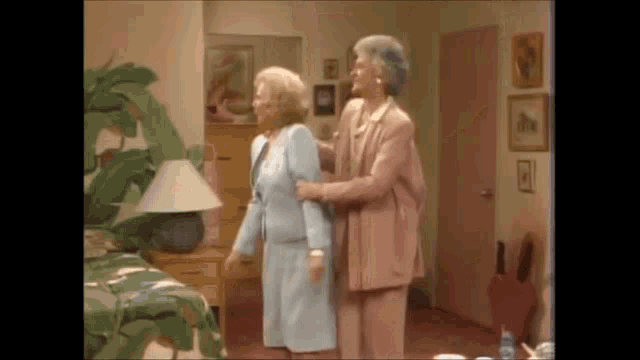two older women are standing next to each other in a room .