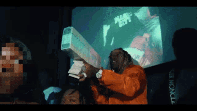 a man in an orange jacket is holding a large stack of money in front of a screen that says miami city