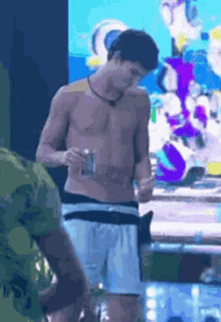a shirtless man in white shorts is standing in front of a large screen holding a drink .