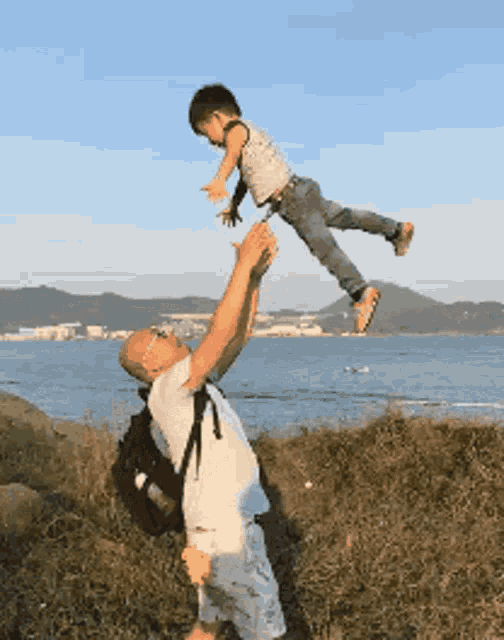 a man is holding a child in the air over a body of water .