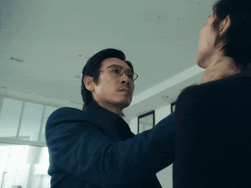 a man in a blue suit and glasses holds another man 's neck