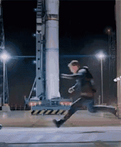 a man is running in front of a rocket in a dark room