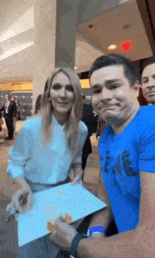 a man in a blue shirt is holding a piece of paper in front of a woman in a white shirt .
