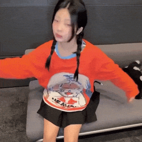 a girl is sitting on a couch with her arms outstretched and wearing a red sweater .
