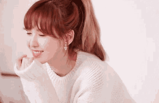 a woman with red hair is wearing a white sweater and earrings and smiling .