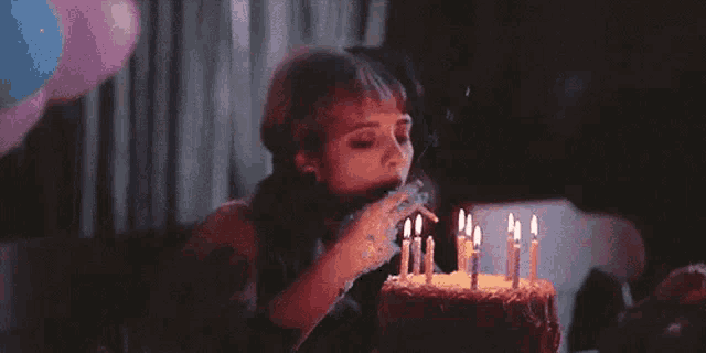 a woman is blowing out candles on a birthday cake and smoking a cigarette .
