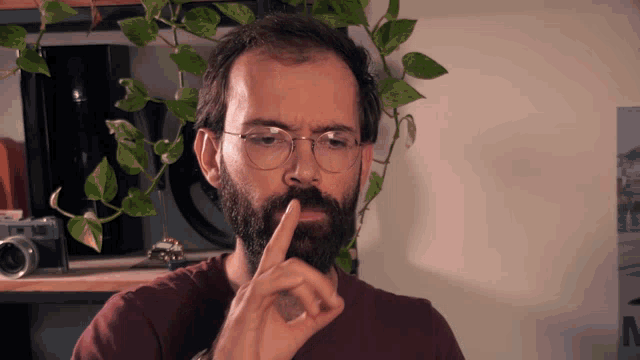 a man with glasses and a beard has his finger on his mouth