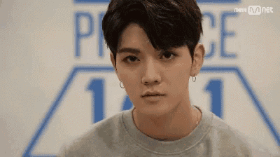 a close up of a young man wearing a gray sweatshirt and earrings .