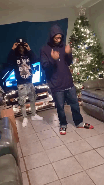 two men are standing in front of a christmas tree and one is wearing a shirt that says bun on it