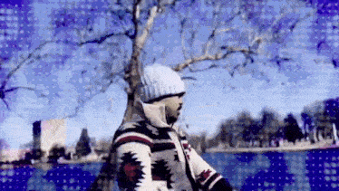 a man in a sweater and hat is standing next to a lake .