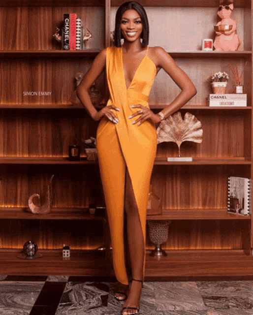 a woman in a yellow dress is standing in front of a bookshelf that has chanel on it