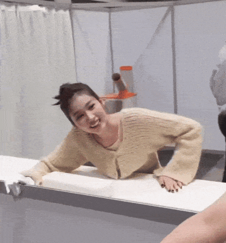 a woman in a tan sweater is laying on a table and smiling