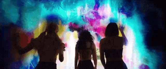 a group of people are dancing in front of a colorful background in a dark room .