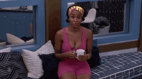 a woman in a pink tank top and shorts is sitting on a couch holding a cup of coffee .