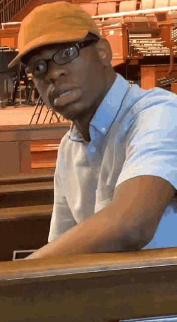 a man wearing glasses and a yellow hat is sitting at a piano