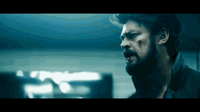 a close up of a man with a beard and blood on his face in a dark room .