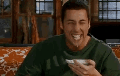a man is sitting on a couch eating a bowl of cereal with a spoon .