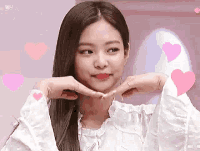 a woman is making a heart shape with her hands while wearing a white shirt .