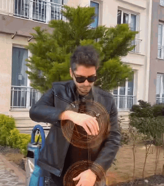 a man wearing sunglasses and a leather jacket is standing in front of a tree