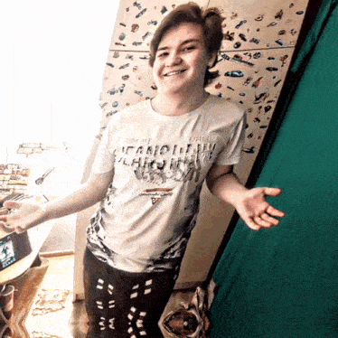 a young man wearing a t-shirt that says ' vanquish ' on it is standing in front of a refrigerator