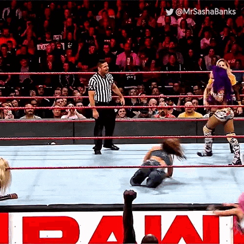 a female wrestler is laying on the ground in a wrestling ring while a referee stands behind her